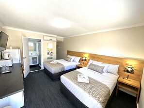 A hotel room with two beds, a desk, a mirror, and a small kitchenette.