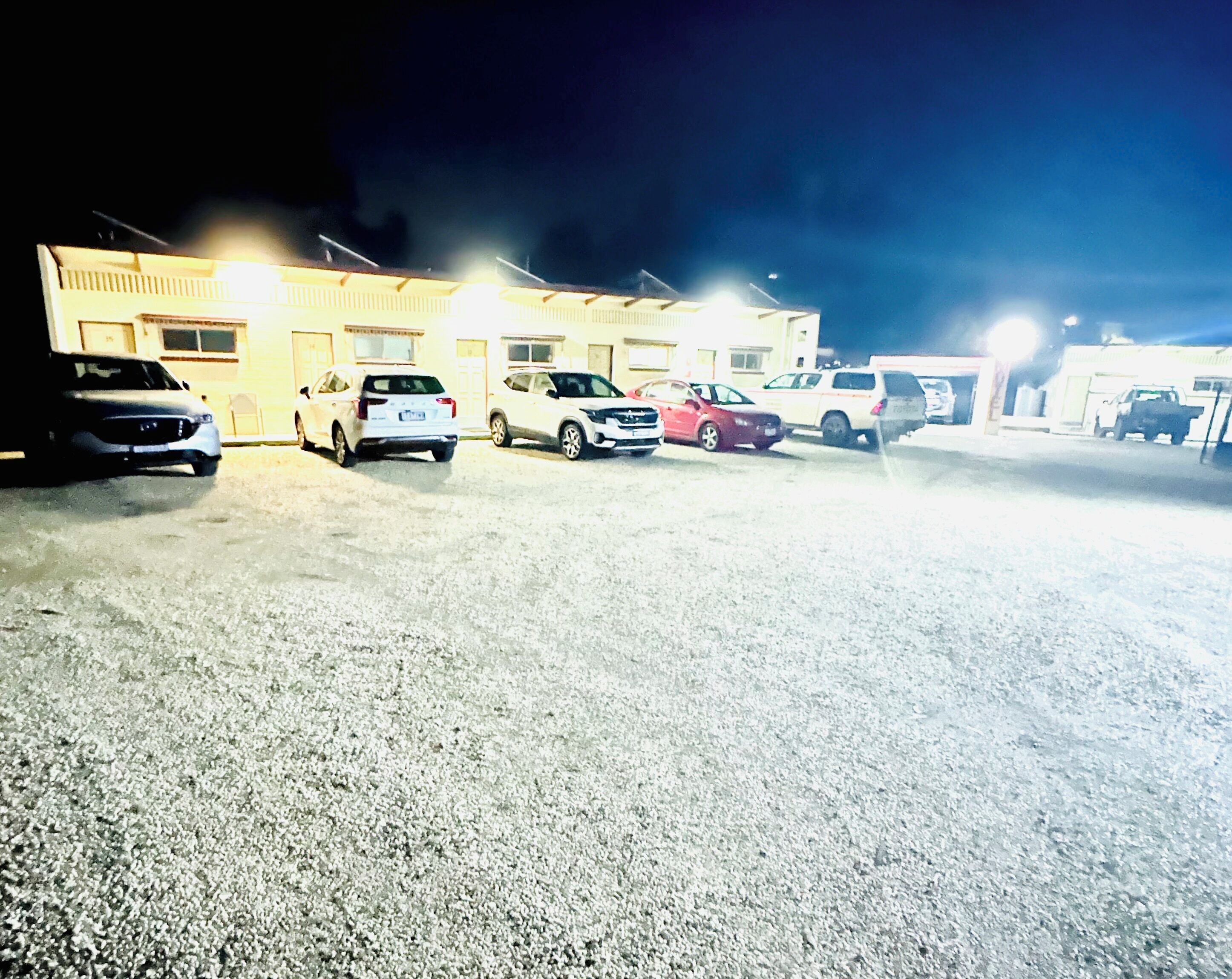 En parkeringsplads med flere biler parkeret foran en bygning om natten.