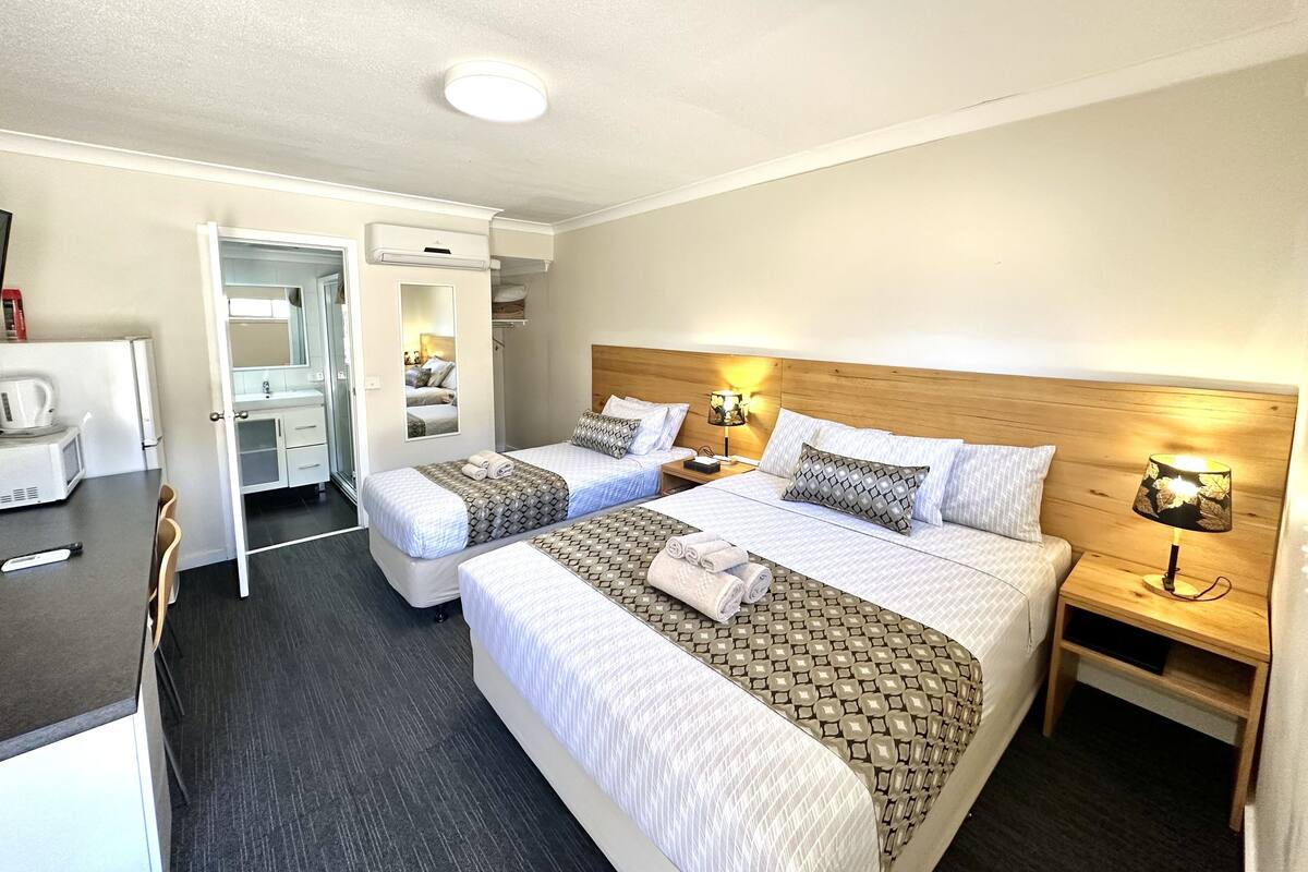 Quarto de hotel com duas camas, uma escrivaninha e uma cozinha compacta.