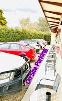 Un estacionamiento con varios autos, mesas al aire libre y un edificio con sección techada.
