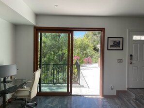 Una habitación con puerta de vidrio que da a un balcón, un escritorio con una silla y un cuadro en la pared.