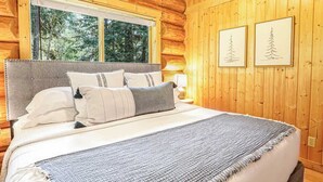 A log cabin bedroom with a bed, window, and two framed pictures on the wall. - Stargazer Lodge | Hot Tub + Game Loft (Glacier)