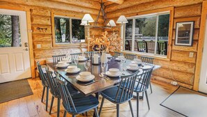 A wooden cabin interior with a dining table set for six, a chandelier, and large windows. - Stargazer Lodge | Hot Tub + Game Loft (Glacier)