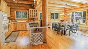 A log cabin interior with a kitchen, dining area, and large windows. - Stargazer Lodge | Hot Tub + Game Loft (Glacier)