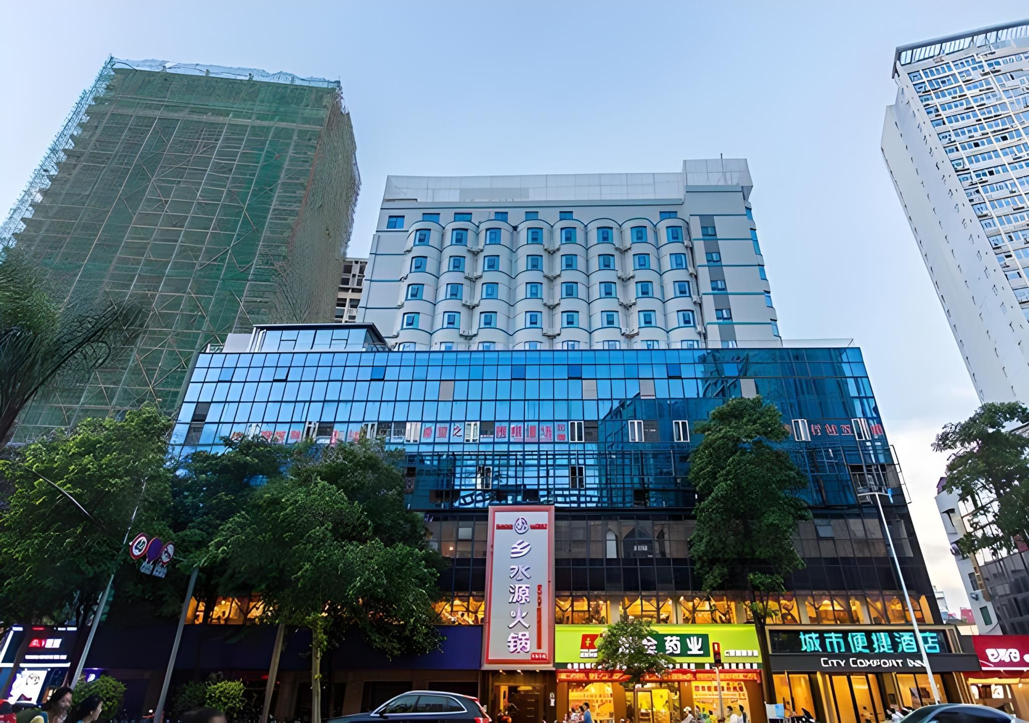 Un hôtel à plusieurs étages doté d’une façade moderne en verre, entouré d’autres immeubles de grande hauteur.
