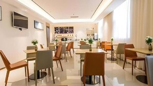 Ein moderner Essbereich mit Tischen und Stühlen, eine Küche im Hintergrund und ein an der Wand befestigter Fernseher.