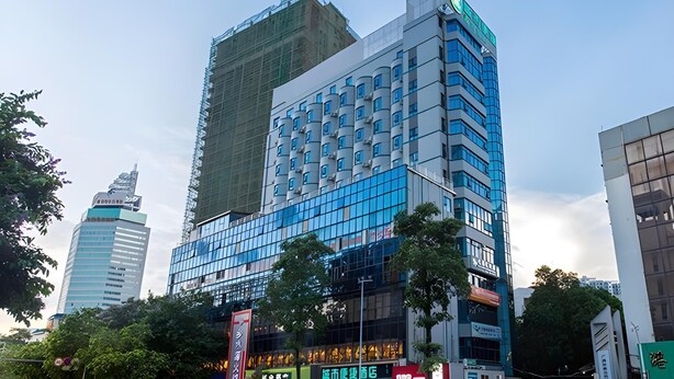 Ein mehrstöckiges Hotel mit moderner Glasfassade, umgeben von anderen Gebäuden.