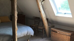 Ein Schlafzimmer im Loftsstil mit schrägen Wänden, einem hölzernen Bett, einem Sessel, einem Schminktisch und einer Weidenholz-Kommode.