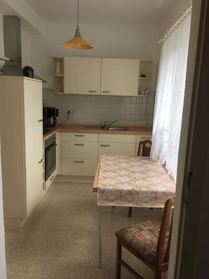 Une petite cuisine équipée d’un seul évier, d’une cuisinière et d’une table recouverte d’une nappe en dentelle.