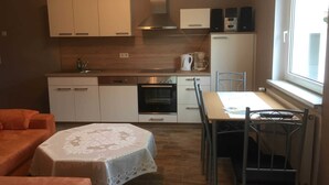 Uma cozinha compacta com armários brancos, forno embutido, cafeteira e uma área de jantar com mesa e cadeiras.