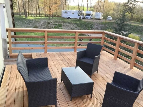 A wooden deck with wicker furniture and a railing overlooking a grassy area with parked vehicles.