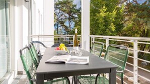 Un balcone con un tavolo apparecchiato per due persone, con una bottiglia, bicchieri e una ciotola di frutta.