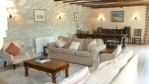 A cozy living room with a stone wall, wooden beams, a sofa set, and a dining area with chairs and a table. - Beautiful, spacious & fully renovated house in the Dordogne (Saint-Cybranet)