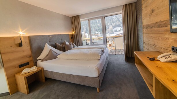 Una habitación de hotel moderna con una cama grande, una mesita de noche y vistas a un paisaje nevado.