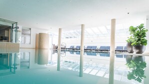 Piscina interior con paredes de vidrio transparente, sillas de descanso y plantas en macetas.