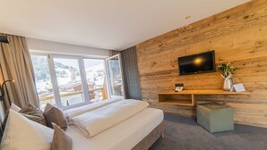 Un dormitorio con una cama grande, un televisor montado en una pared de madera y vistas a un paisaje nevado a través de un ventanal amplio.