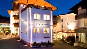 Un edificio blanco con letreros de 'HOCHLAND', balcones con plantas y una entrada bien iluminada.