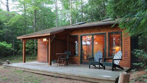 A wooden cabin with a deck, large windows, and two Adirondack chairs. - Adirondack Riverfront Retreat (Jay)