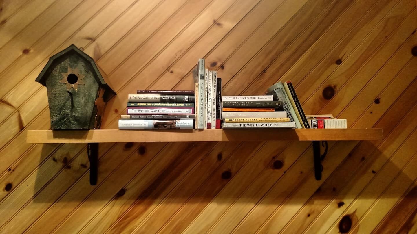 Une bibliothèque en bois, avec des livres et une nichoir, adossée à un mur en bois.