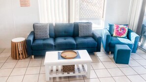 A living room with a blue sofa set, a white coffee table, and a round wooden stool.
