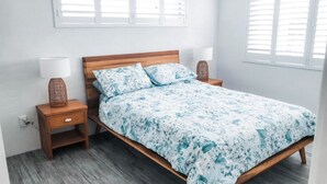 Une chambre à coucher avec un lit en bois, deux tables de chevet et une fenêtre avec des stores.
