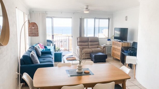 Un salon moderne avec un canapé, une table à manger, un téléviseur et un balcon offrant une vue agréable.