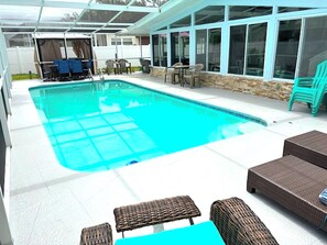 A swimming pool with a covered area, wicker furniture, and a stone wall.