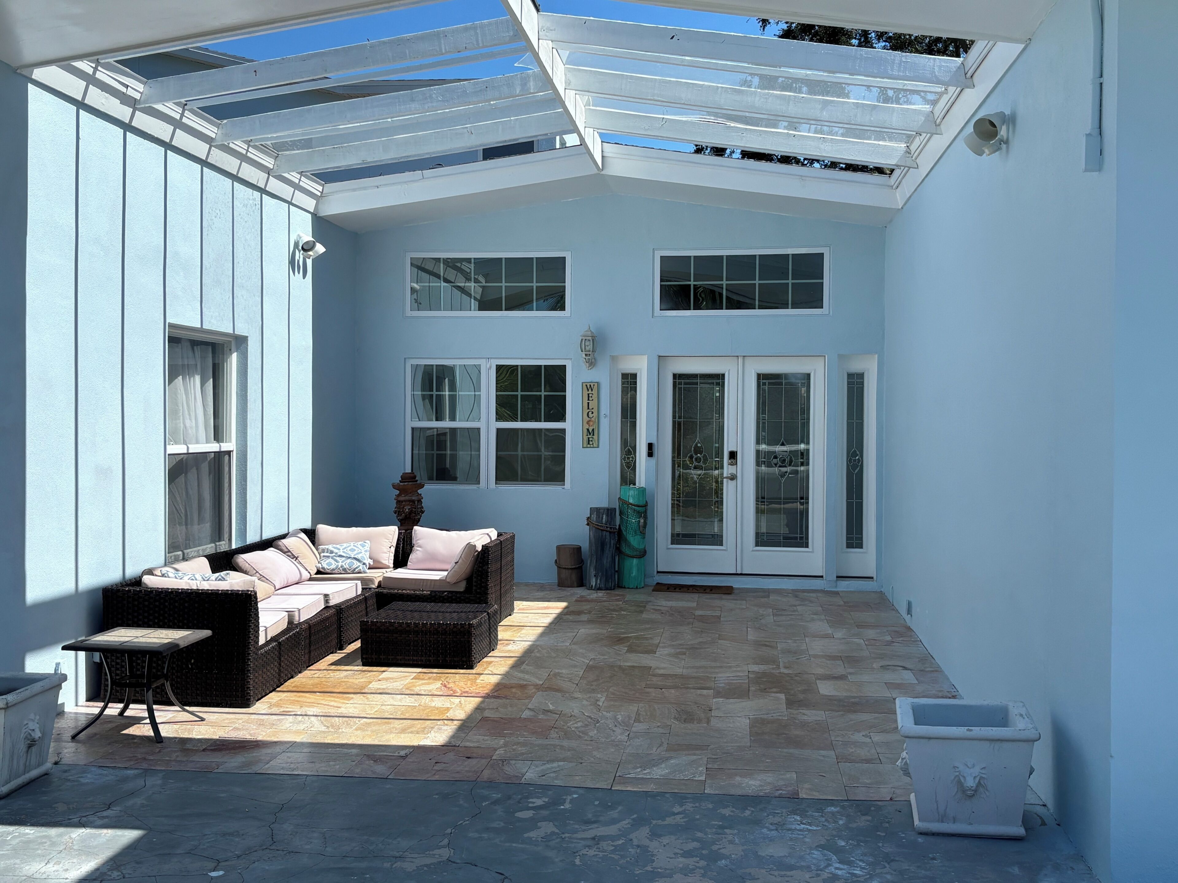 A covered patio with a seating area, a door with glass panels, and a wall-mounted security camera.