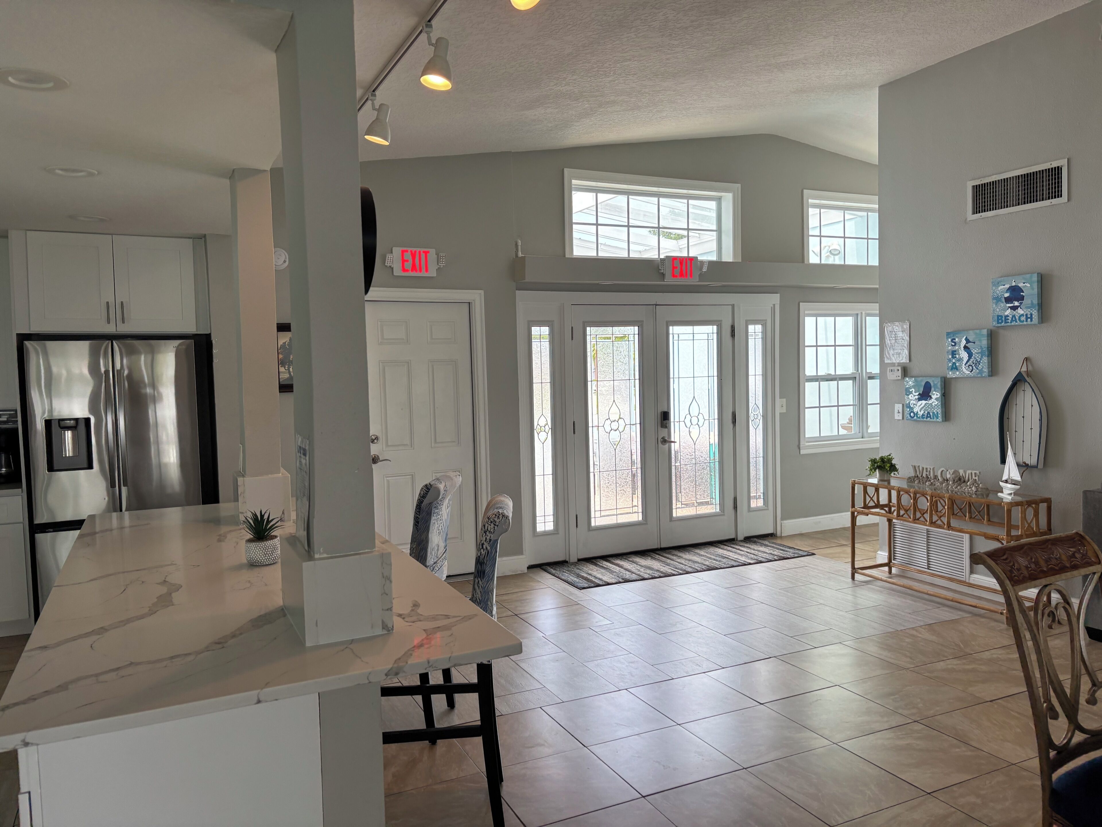 A spacious kitchen with a large island, a stainless steel refrigerator, and a double door entrance.