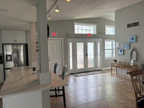A spacious kitchen with a large island, a stainless steel refrigerator, and a double door entrance.