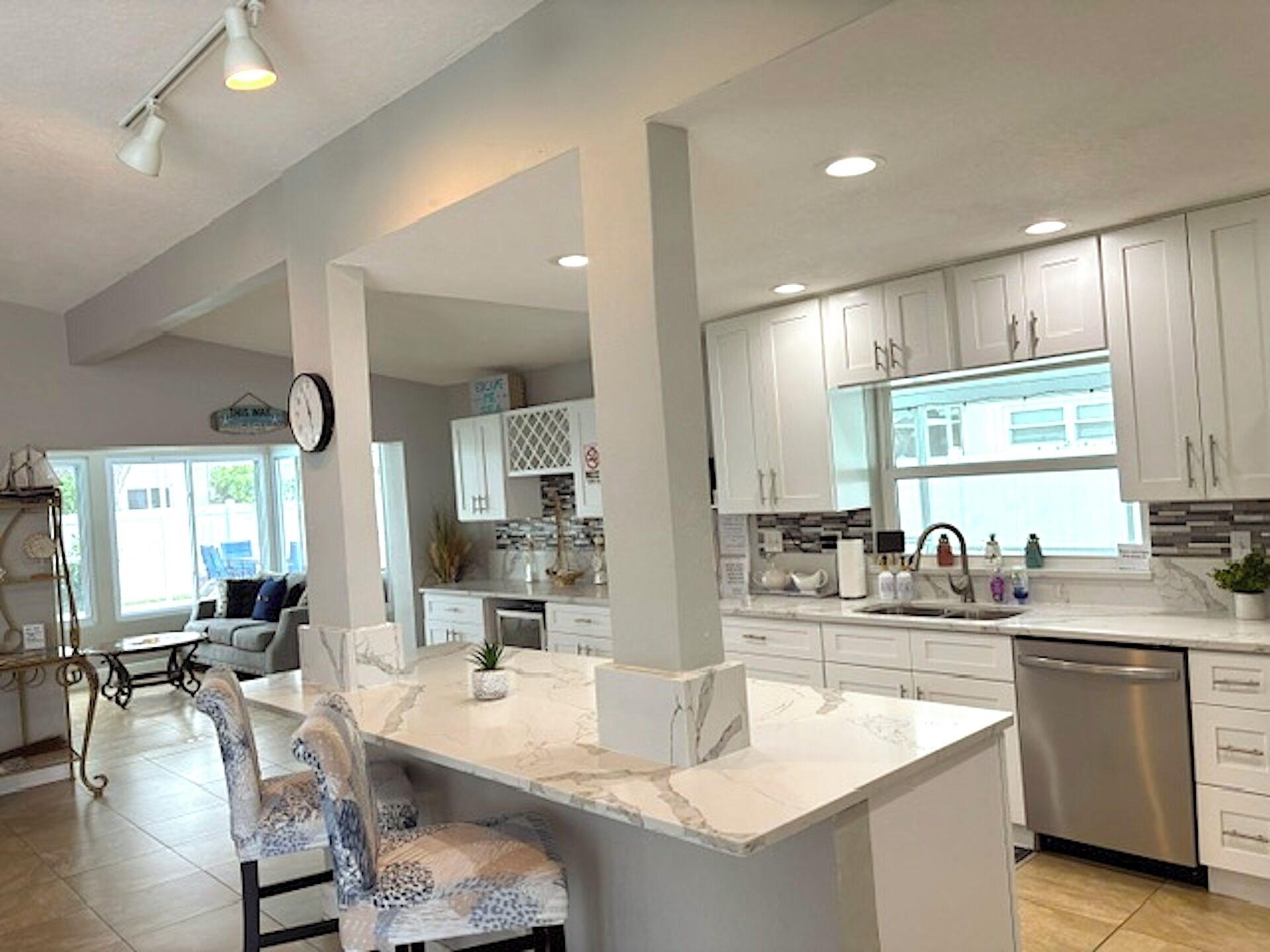 A modern kitchen with white cabinetry, a marble island, and a stainless steel dishwasher.
