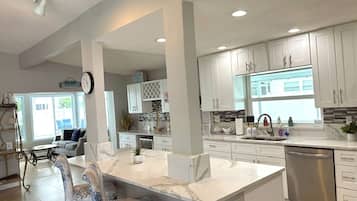 A modern kitchen with white cabinetry, a marble island, and a stainless steel dishwasher.