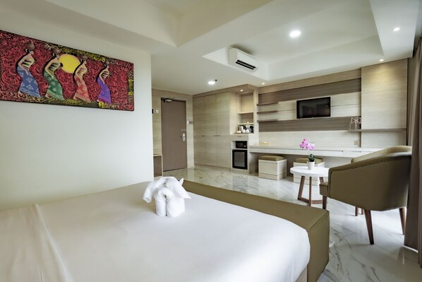 Habitación de hotel con cama, escritorio, silla, televisor y zona de cocina.