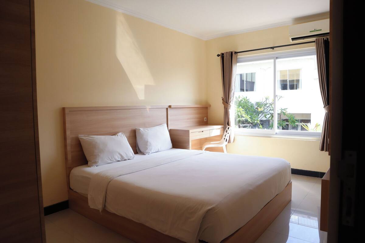 A hotel room with a large bed, a desk, and a window with curtains.