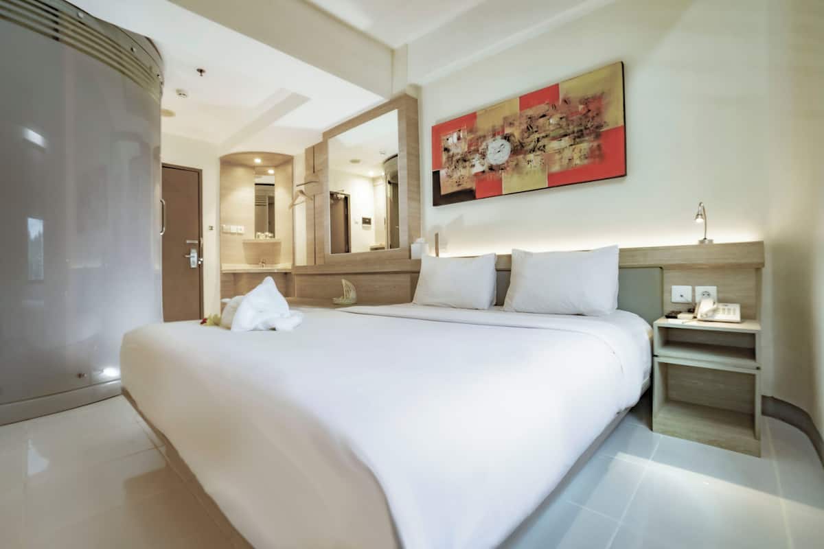 A modern hotel room with a large bed, a bedside table with a lamp, a mirror, and a wall-mounted artwork.