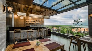 A modern kitchen with a bar area, wooden furniture, and a large window overlooking a scenic view. - Sunrise Aventus Hotel Nusa Dua (Nusa Dua)