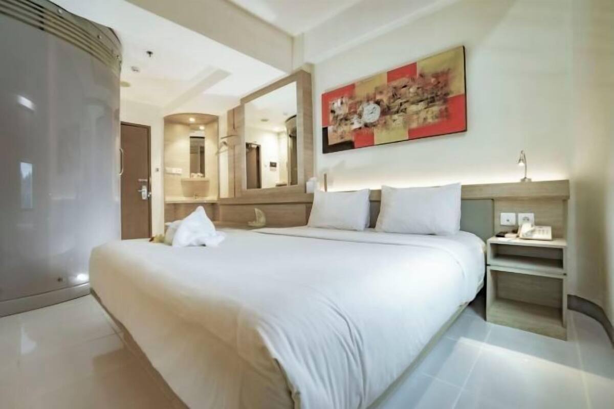 A hotel room with a large bed, a bedside table, a nightstand, a mirror, and a painting on the wall.