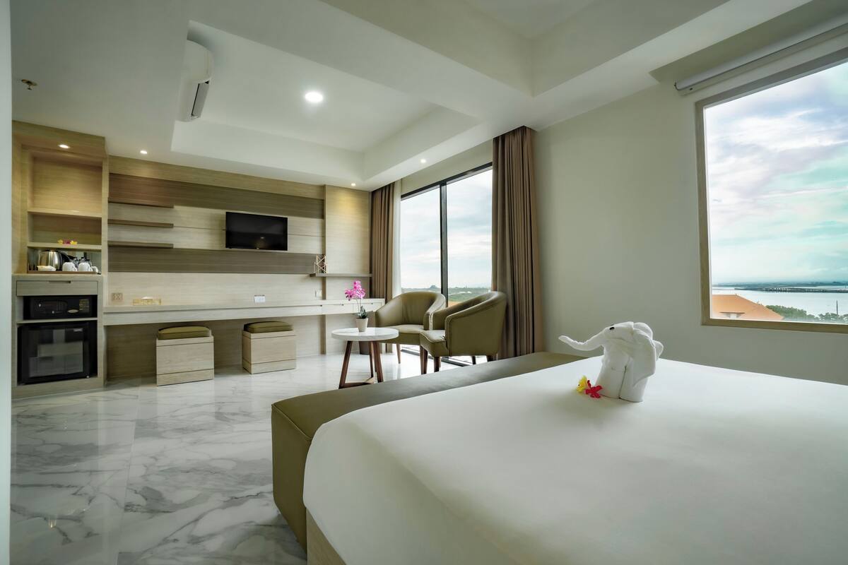 A hotel room with a bed, a desk, a chair, a TV, and a view of the sea.