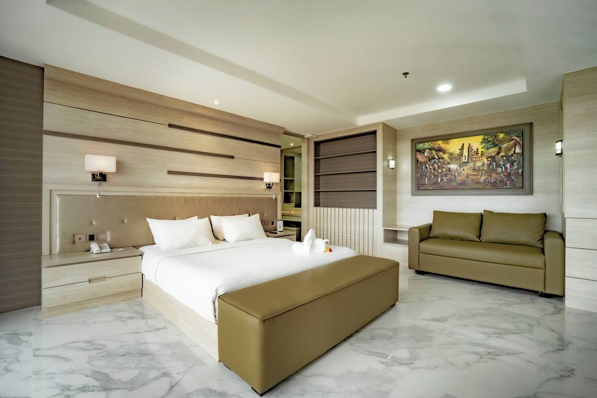 A modern hotel room with a large bed, a sofa, a marble floor, a painting on the wall, and a wooden headboard.