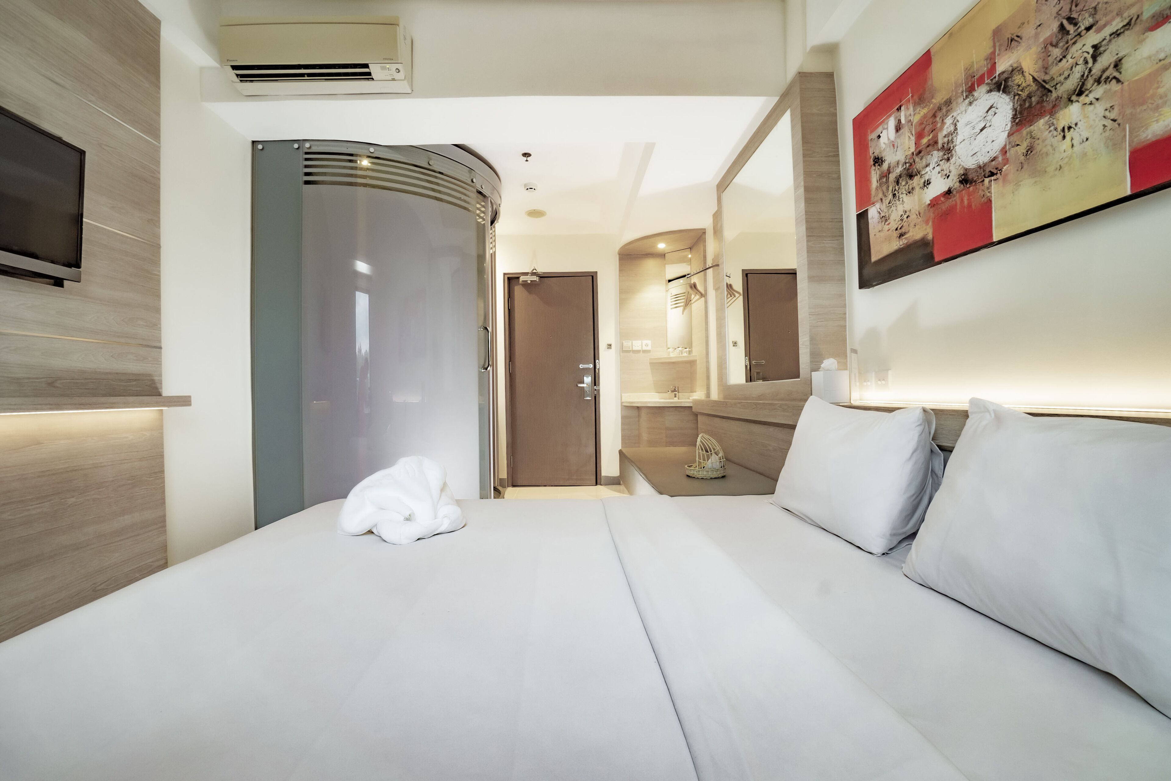 Habitación de hotel moderna con cama, televisión de pantalla plana, zona de ducha y un cuadro abstracto grande en la pared.