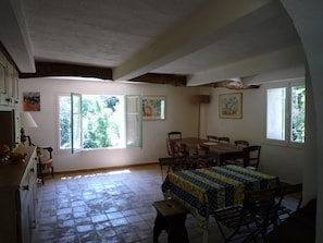 A dining area with a table and chairs, a kitchen with cabinets and a stove, and a large window with a view of trees. - 18th-century Provencal country house on the banks of the Argens river, set in 2 ha of land (Le Thoronet)