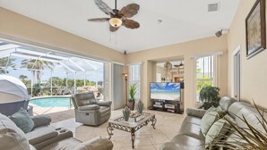 Un vaste espace de vie avec piscine, des canapés en cuir, un téléviseur et un ventilateur de plafond.
