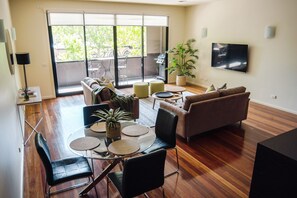 Un soggiorno moderno con un tavolo da pranzo in vetro, due divani, una TV e una porta scorrevole in vetro che si apre sull'esterno.