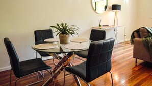 A modern living room with a glass dining table surrounded by black leather chairs, a potted plant, and a round mirror on the wall. - Spacious, modern apartment right in the Bendigo CBD (Bendigo)