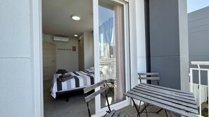 Un balcón con banco y mesa de madera, una cama con ropa de cama a rayas y vistas al exterior.