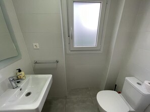 A small bathroom with a white sink, toilet, and a window above the door.
