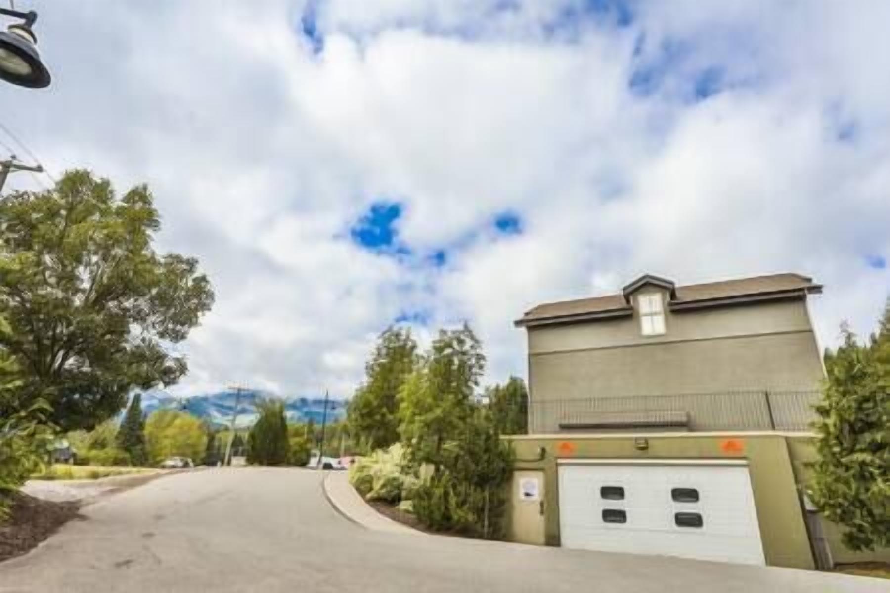 Una strada residenziale con un garage, alberi e un cielo nuvoloso.