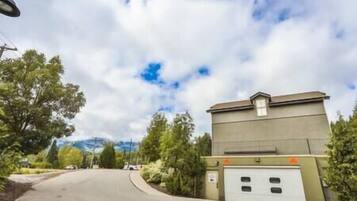 Una strada residenziale con un garage, alberi e un cielo nuvoloso.