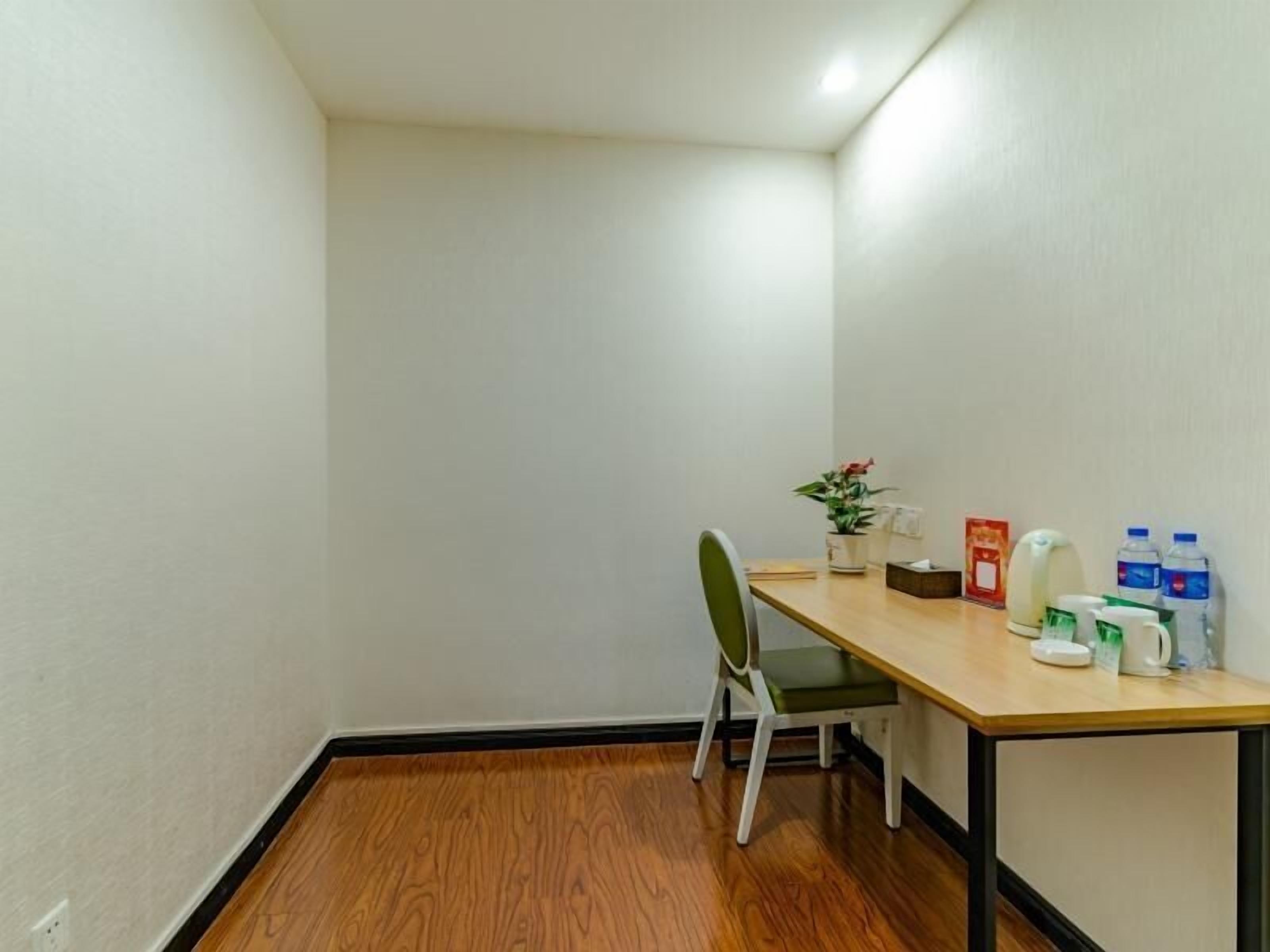 Une petite pièce propre, avec un plancher en bois, une seule chaise, une table sur laquelle est posée une plante en pot, et quelques articles de toilette.