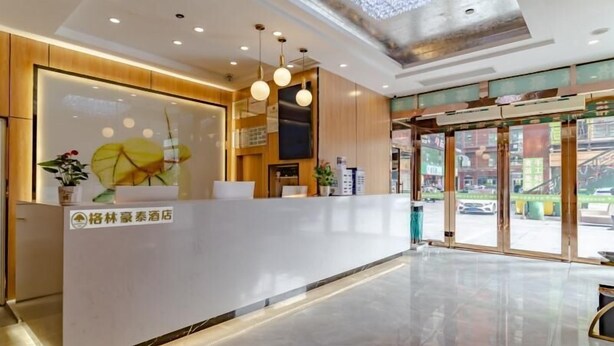 A modern hotel reception area with a white reception desk, wooden paneling, and a large window offering a view of the street.